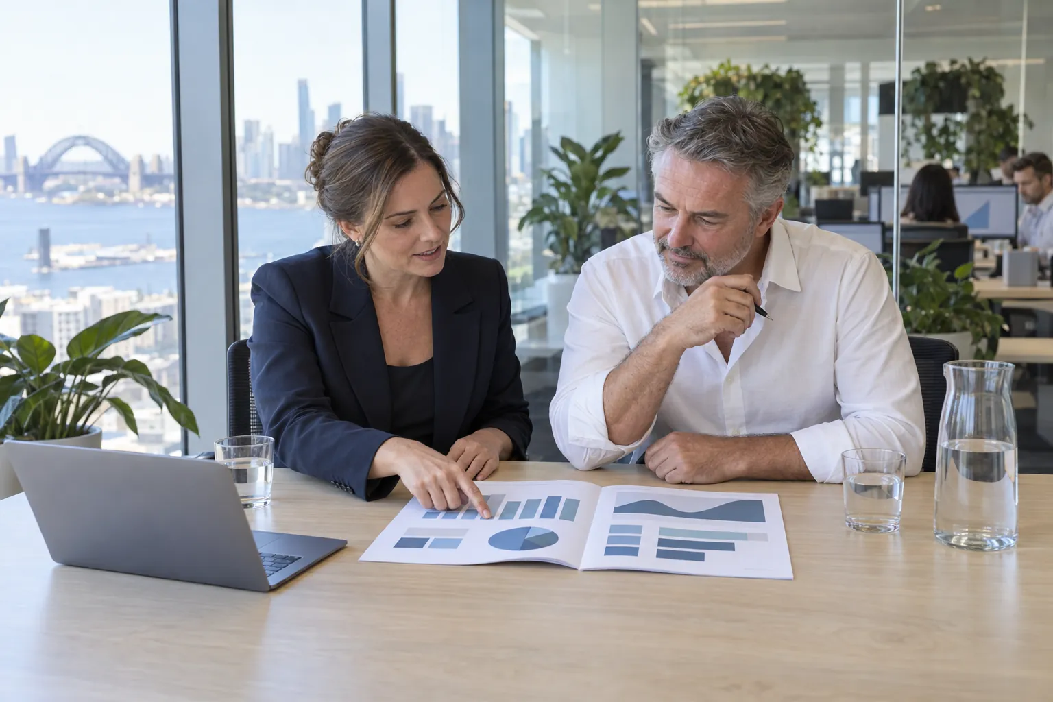 A facility manager and an asset manager going through a printed monthly report at a table in a glass-walled meeting room.