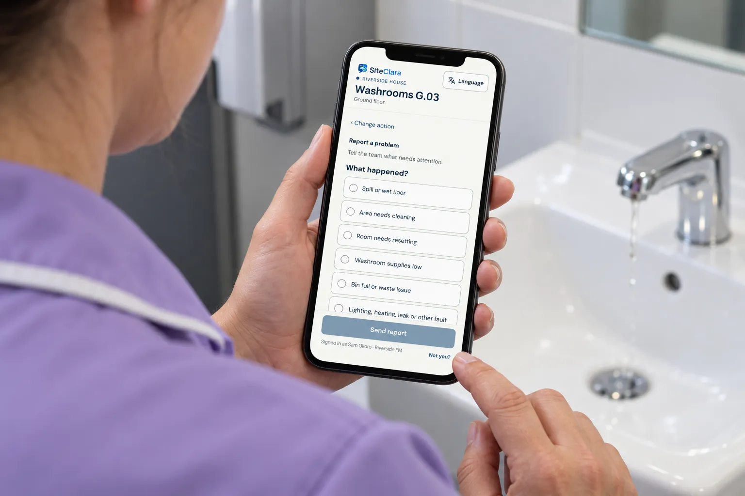 A cleaner reporting a dripping tap on a phone app in a washroom.