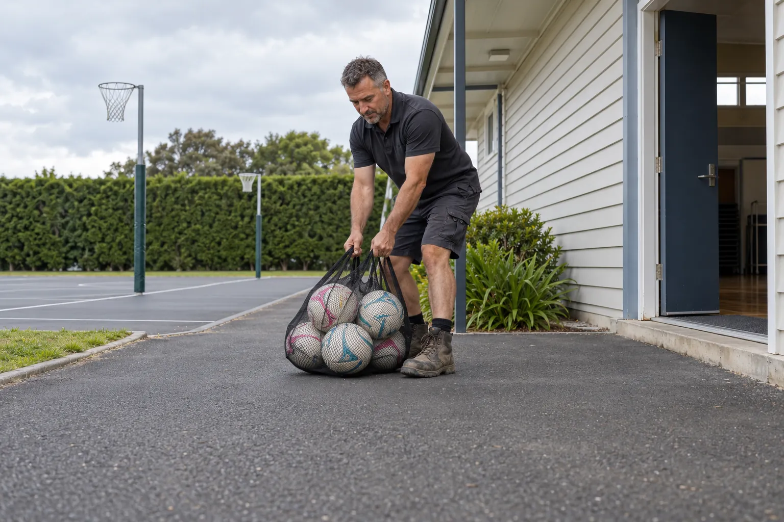 A caretaker clearing a bag off the path outside a school hall.